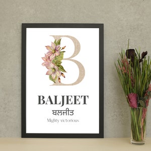May include: A framed art print with the name "BALJEET" in black, with a floral "B" and text in a second language. The print also includes the phrase "Mighty victorious". A vase of flowers is positioned to the right of the framed print.