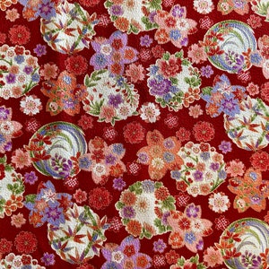 May include: Red fabric with a repeating pattern of white, pink, and purple flowers and gold accents. The fabric has a textured surface.