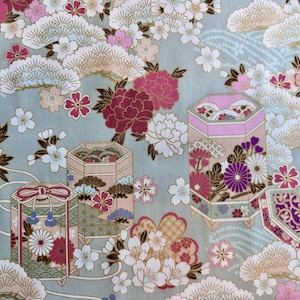 Puede incluir: Una tela azul claro con un patrón repetitivo de flores rosas y blancas, acentos dorados y pequeñas cajas con diseños florales.