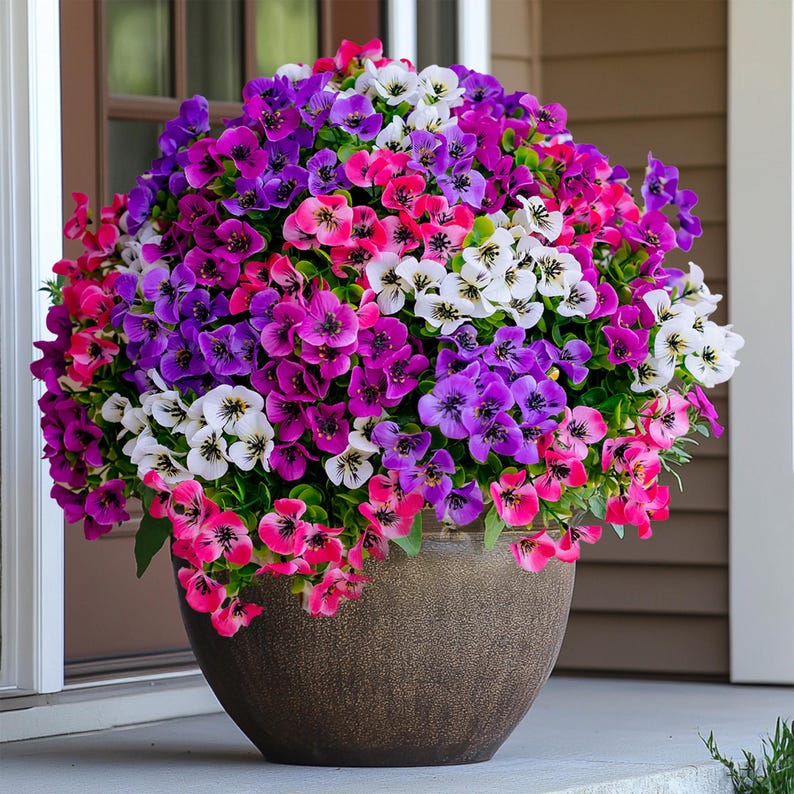 May include: A brown pot filled with a variety of colorful flowers. The flowers are pink, purple, and white. The pot is sitting on a porch.
