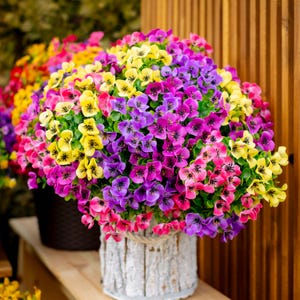 May include: A bouquet of artificial flowers in a white planter. The flowers are a mix of purple, pink, and yellow.