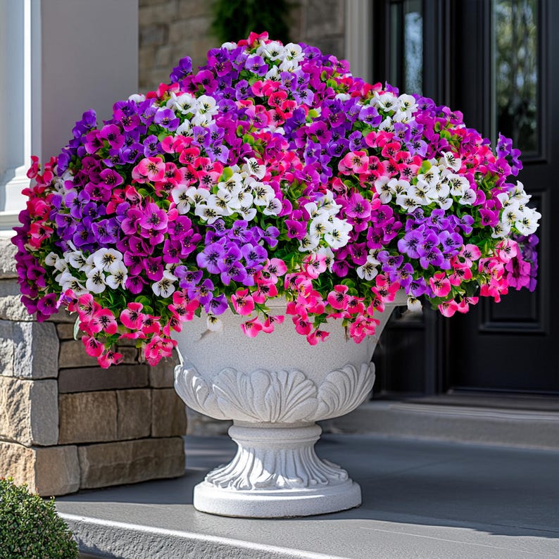 May include: A white ceramic planter with a decorative design holds a vibrant mix of pink, purple, and white flowers. The flowers are in full bloom and create a beautiful display.