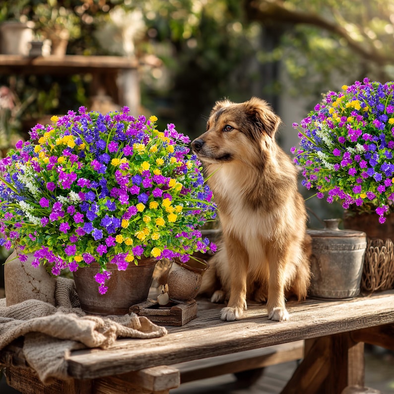 May include: A wooden table displays vibrant, colorful faux flower arrangements in metal pots. The flowers are a mix of purple, yellow, and blue. A brown and tan dog sits on the table, looking to the side.