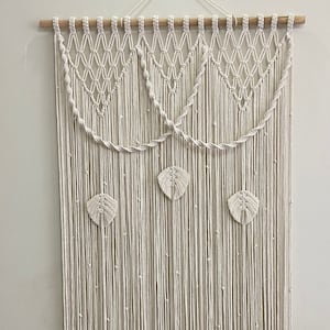 Peut inclure: Une suspension murale en macramé blanche avec un motif géométrique et des motifs de feuilles. La suspension est faite de cordon de coton et mesure environ 90 cm de large et 120 cm de haut.