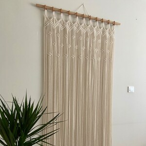 May include: A macrame wall hanging with a geometric pattern, made with natural cotton cord and a wooden dowel rod.