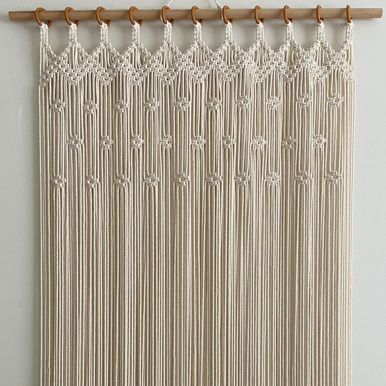 May include: A white macrame wall hanging with a geometric pattern. The hanging is made of cotton cord and is attached to a wooden dowel rod with wooden rings.