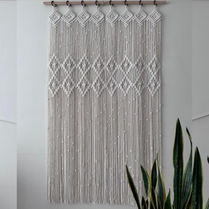 Puede incluir: Un tapiz de macramé blanco con un patrón de diamante. El tapiz está hecho de cordón de algodón y mide aproximadamente 178 cm de largo y 76 cm de ancho.