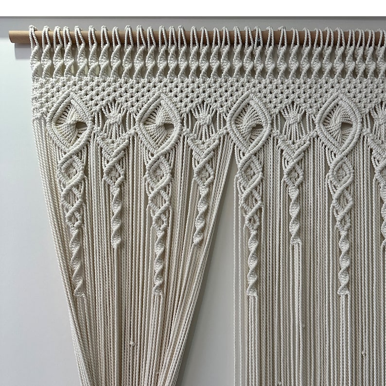 May include: A white macrame wall hanging with a geometric pattern. The hanging is made of cotton cord and is attached to a wooden dowel.