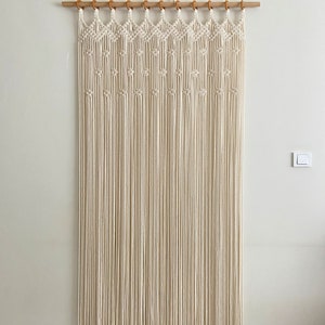 May include: A white macrame wall hanging with a geometric pattern. The hanging is made of cotton cord and is attached to a wooden dowel rod.