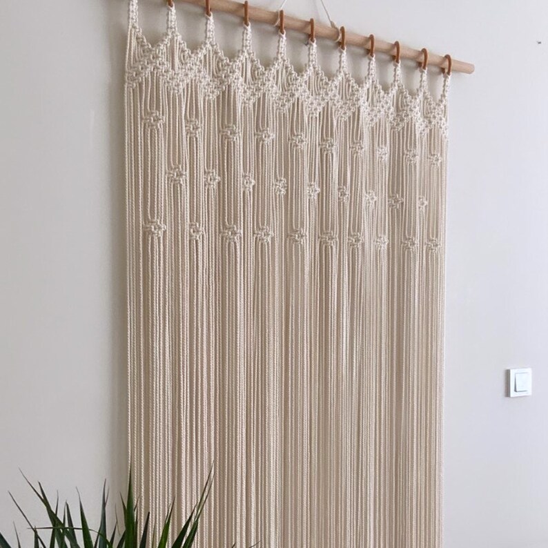 May include: A white macrame wall hanging with a geometric pattern. The hanging is made of cotton cord and is attached to a wooden dowel rod.