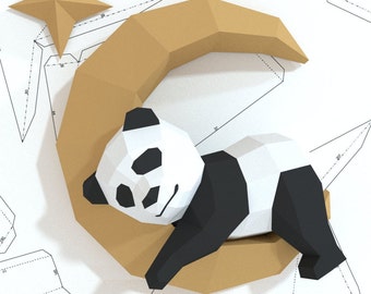 May include: A papercraft model of a panda bear sleeping on a crescent moon. The panda is black and white, and the moon is a light brown color.