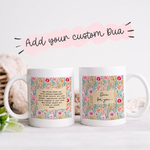 Op de afbeelding: Twee witte keramische mokken met bloemenpatronen. Eén mok heeft een tekstvak met een gebed in Arabisch schrift en de woorden "Moge Allah je zegenen met eindeloos geluk. Moge Allah al je dromen, aspiraties en gebeden vervullen. Moge Allah je gebeden verhoren. Moge Allah je belonen met een huis in het Paradijs. Amin". De andere mok heeft een tekstvak met de woorden "Dua voor jou...".