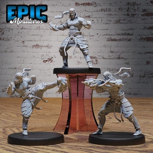 May include: Three gray plastic figurines of martial artists in fighting poses. The figures are on black bases and one is on a clear red stand. The figures are all wearing headbands and have a muscular build.