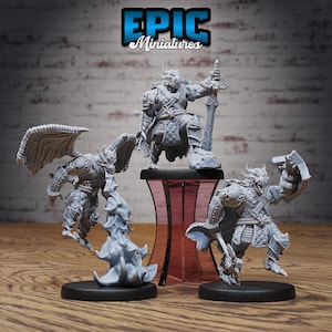 Può includere: Tre miniature dipinte di grigio raffiguranti creature simili a draghi, ciascuna con una posa e un'arma diversa. Le miniature sono su basi nere e sono esposte su un supporto rosa e nero. Il testo "EPIC Miniatures" è visualizzato nella parte superiore dell'immagine.