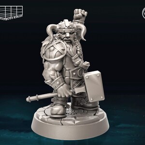 May include: A gray, 3D printed miniature of a dwarf warrior with a beard, wearing a helmet and armor, holding a hammer and a shield. The miniature is standing on a round base.
