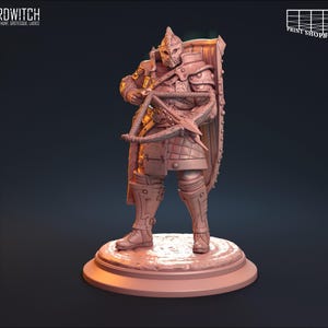 Puede incluir: Una figura en miniatura de un guerrero con armadura y casco, sosteniendo una ballesta. La figura está de pie sobre una base redonda.