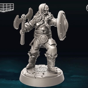 Puede incluir: Una figura miniatura de plástico gris de un guerrero con barba, sosteniendo un hacha y un escudo. La figura está de pie sobre una base redonda con un diseño circular.