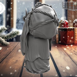 以下が含まれることがあります： フード付きのローブを着て、大きな包みを運んでいる人のグレーの3Dプリントされたフィギュア。フィギュアは、雪の降る冬のシーンがぼやけて見える木製の表面に立っています。