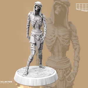 Könnte beinhalten: Eine weiß bemalte Miniaturfigur eines Skeletts, das eine Kapuzenrobe und Bandagen trägt. Die Figur steht auf einem runden Sockel.