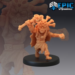 May include: A small, detailed, beige-coloured figurine of a goblin-like creature with a skull headdress and a bone club. The creature is wearing a loincloth and has a fierce expression.