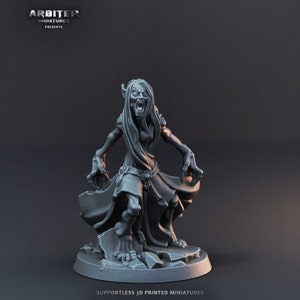 Op de afbeelding: Een 3D-geprint miniatuur van een goblinoid wezen met een woeste uitdrukking, dat een lange robe draagt en op een rotsachtige basis staat. Het miniatuur is grijs en ongeverfd.