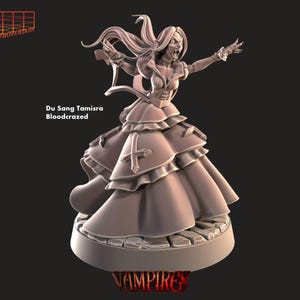 May include: A detailed miniature figurine of a vampire woman in a flowing gown, with a cross on her chest. The figurine is painted in shades of grey and has a textured base. The text "Du Sang Tamisra Bloodcrazed" is printed below the figurine.