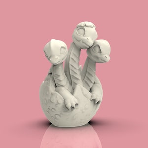 Könnte beinhalten: Eine weiße Keramikfigur eines dreiköpfigen Drachen, der aus einem Ei schlüpft. Der Drache hat große Augen und einen niedlichen Ausdruck.