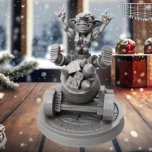 Puede incluir: Una figura gris impresa en 3D de una criatura parecida a un duende montada en un carro lleno de cajas de regalo. La figura tiene los brazos levantados y está sobre una base circular. El fondo incluye decoraciones navideñas y el texto "PRINT SHOP BOYS" y "Cast n Play".