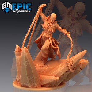 Puede incluir: Una figura en miniatura de una persona con una cara esquelética, que lleva una túnica desgarrada y sostiene dos cadenas. La figura está de pie sobre una base rocosa.