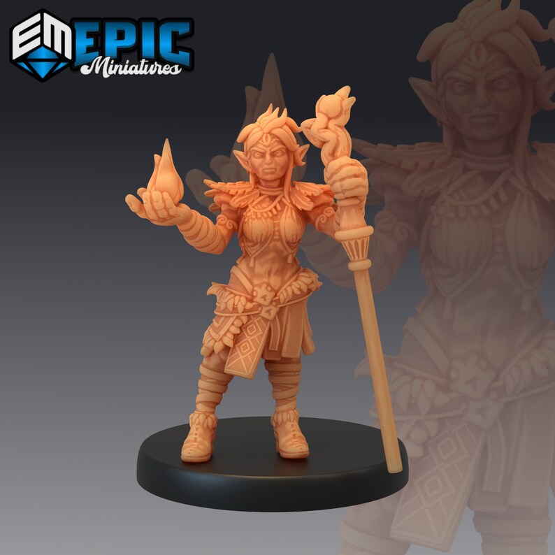 May include: A miniature figurine of a female elf warrior, painted in a light brown colour. She is wearing armour and holding a staff with a flame at the top. The figurine is standing on a round base.