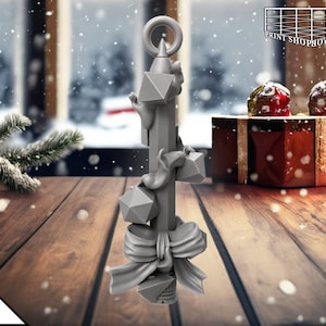 Könnte beinhalten: Ein grauer, 3D-gedruckter Weihnachtsbaumschmuck in Form eines Bleistifts mit Schleife und geometrischen Formen. Der Schmuck liegt auf einer Holzoberfläche.