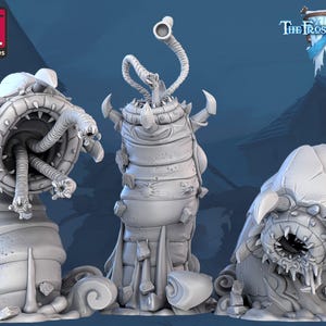 May include: Three 3D printed grey and white miniature creatures with a worm-like appearance. The creatures have large mouths with teeth and tentacles. The creatures are on a grey background. The text "The Frost City" is visible in the background.