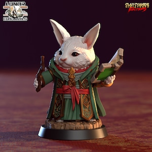 Puede incluir: Un conejo blanco con una túnica verde y dorada con una faja roja, sosteniendo una botella en una mano y un libro en la otra. El conejo está de pie sobre una base negra.