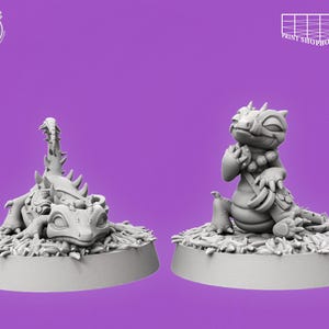 Puede incluir: Dos figuras de dragones grises sobre un fondo morado. Un dragón está tumbado, el otro está sentado. Ambos están sobre una base con textura de hierba. Los textos "Cast n Play" y "Print Shop Boys" son visibles.