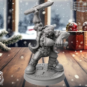 Könnte beinhalten: Graue Figur einer Fantasy-Figur, die ein Schwert über dem Kopf und eine Tasche hält. Die Figur steht auf einem runden Sockel mit strukturierter Oberfläche. Der Hintergrund umfasst eine verschneite Szene und eine Geschenkbox mit roten und weißen Dekorationen. Die Figur ist von Cast n Play.