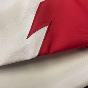 May include: A close-up of a white fabric with a red lightning bolt design. The fabric is folded over, showing the underside of the fabric.