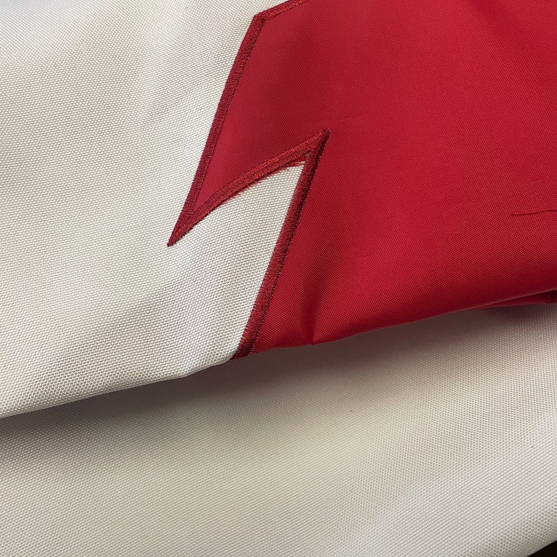 May include: A close-up of a white fabric with a red lightning bolt design. The fabric is folded over, showing the underside of the fabric.
