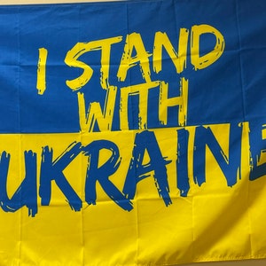 Puede incluir: Una bandera azul y amarilla con las palabras "I Stand With Ukraine" escritas en pintura azul.