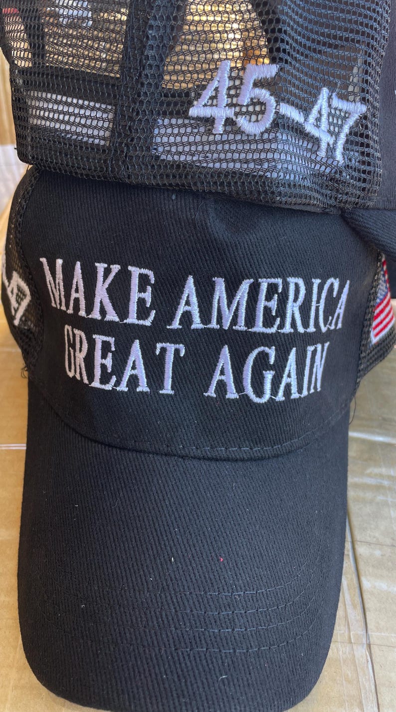 May include: Black baseball cap with the phrase "MAKE AMERICA GREAT AGAIN" embroidered in white. The cap has a mesh back and the numbers "45-47" embroidered in white on the mesh.