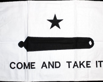 May include: A white flag with a black star and a black cannon with the words "COME AND TAKE IT" printed below.