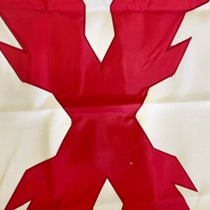May include: A white fabric flag with a large red X in the center. The X is made of two overlapping red triangles with jagged edges.