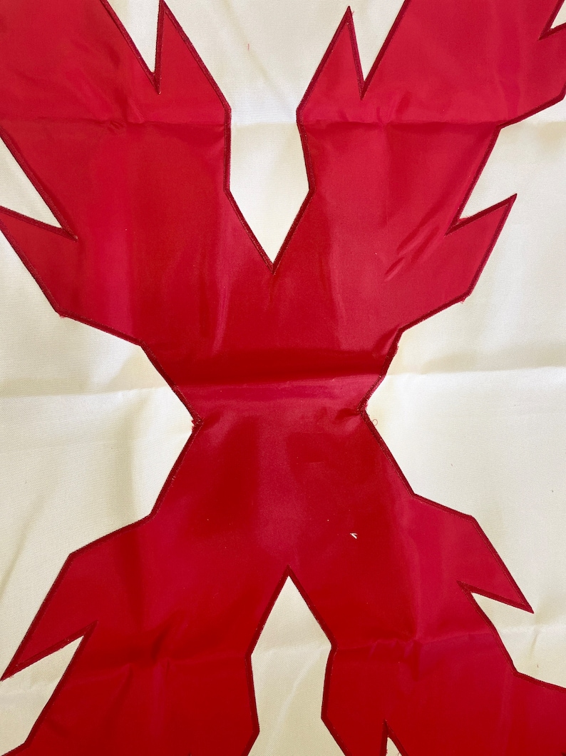 May include: A white fabric flag with a large red X in the center. The X is made of two overlapping red triangles with jagged edges.