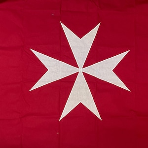 May include: A rectangular flag featuring a solid deep red background with a large, centered white Maltese cross. The cross has eight points, with each arm narrowing toward the center and widening at the ends, creating a distinct geometric shape.