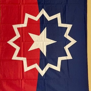 May include: A rectangular flag divided vertically into red on the left and blue on the right. A large white twelve-pointed starburst with a central five-pointed star is centered on the flag. The text June 19, 1865 is printed in white at the bottom.