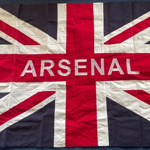 May include: A Union Jack flag with the word "ARSENAL" printed in white across the centre.