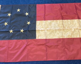 May include: A Confederate States of America flag with a blue field containing 13 gold stars in a circle, a white stripe, and a red stripe.