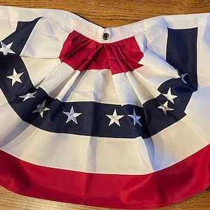 Puede incluir: Una guirnalda de banderines patri&oacute;tica roja, blanca y azul con un dise&ntilde;o plisado. La bandera presenta un borde rojo, un centro blanco y rayas azul marino con estrellas blancas. Tiene ojales para colgar.