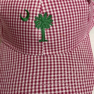 May include: Pink and white gingham baseball cap with a green embroidered palmetto tree and crescent moon.