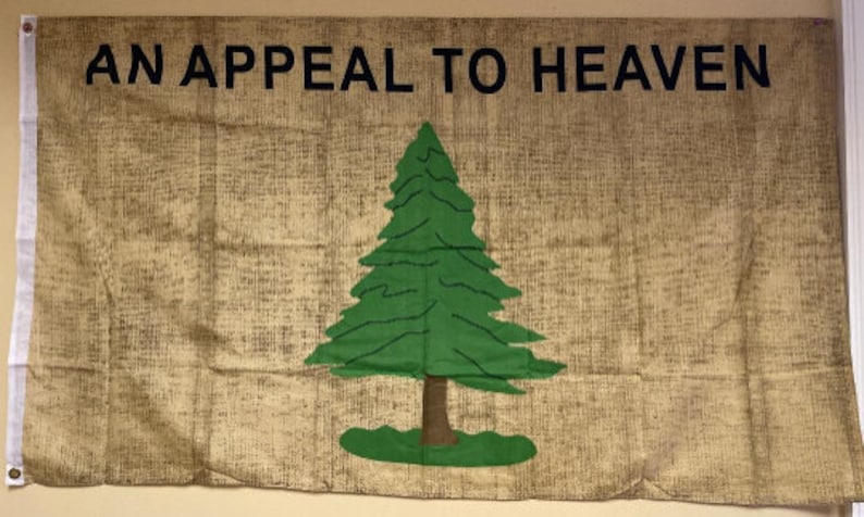 Puede incluir: Una bandera de tela marr&oacute;n con el texto "AN APPEAL TO HEAVEN" en letras negras. Un pino verde est&aacute; centrado en la bandera.