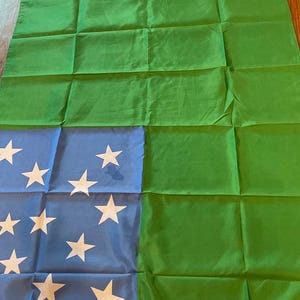 May include: A green and blue flag with white stars. The flag is folded and has a white border at the bottom.
